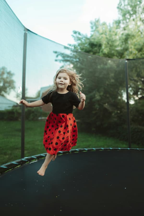 A young girl in a black and red dress rounds on a trampoline.