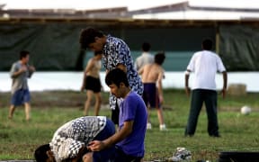 A small group of Muslim refugees pray at sunset while other refugees (background) participate in a football match at a camp for the asylum seekers on the small island of Nauru, 20 September 2001.