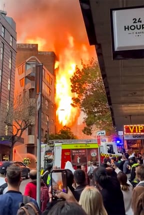 This screen grab from a UGC video taken and posted by Grant Ozolins on the Twitter account @grantozolins on May 25, 2023 shows people watching a fire in central Sydney. More than 100 firefighters battled towering flames and thick smoke from a seven-storey blaze in central Sydney on May 25 that was spreading to other buildings. (Photo by Grant OZOLINS / Twitter/@grantozolins / AFP) / -----EDITORS NOTE --- RESTRICTED TO EDITORIAL USE - MANDATORY CREDIT "AFP PHOTO / Twitter account @grantozolins/ Grant Ozolins  " - NO MARKETING - NO ADVERTISING CAMPAIGNS - DISTRIBUTED AS A SERVICE TO CLIENTS