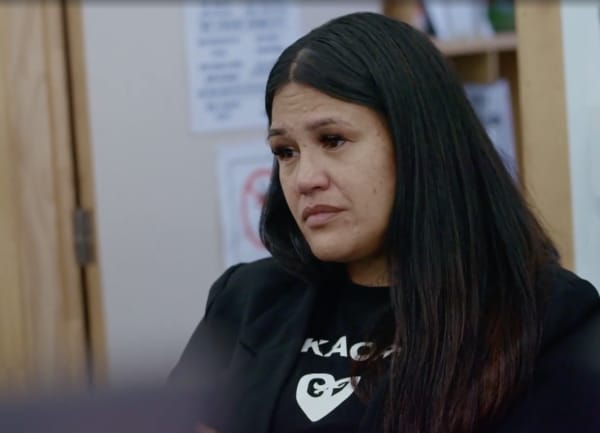 A teary dark-haired woman looks to the side.