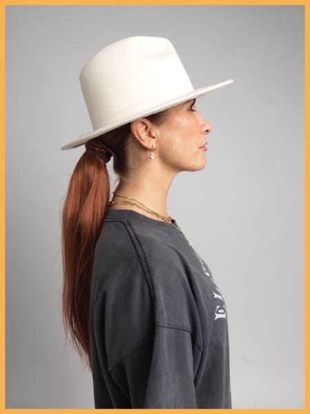 MC Tali stands in profile wearing a grey t-shirt and a white wide-brimmed hat.