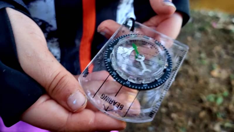 Child learning to use a compass outdoors.