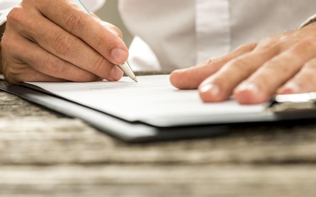 A man in a white business shirt signs a job offer or contract (file)