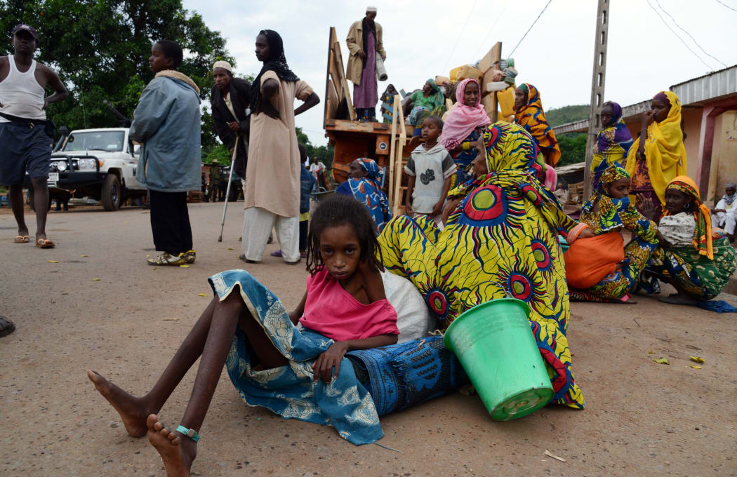 A girl sits on the pavement as a vehicle loaded with people and goods, part of a convoy of vehicles carrying Muslims from the PK12 district, outside of Bangui, gets ready to leave the city.