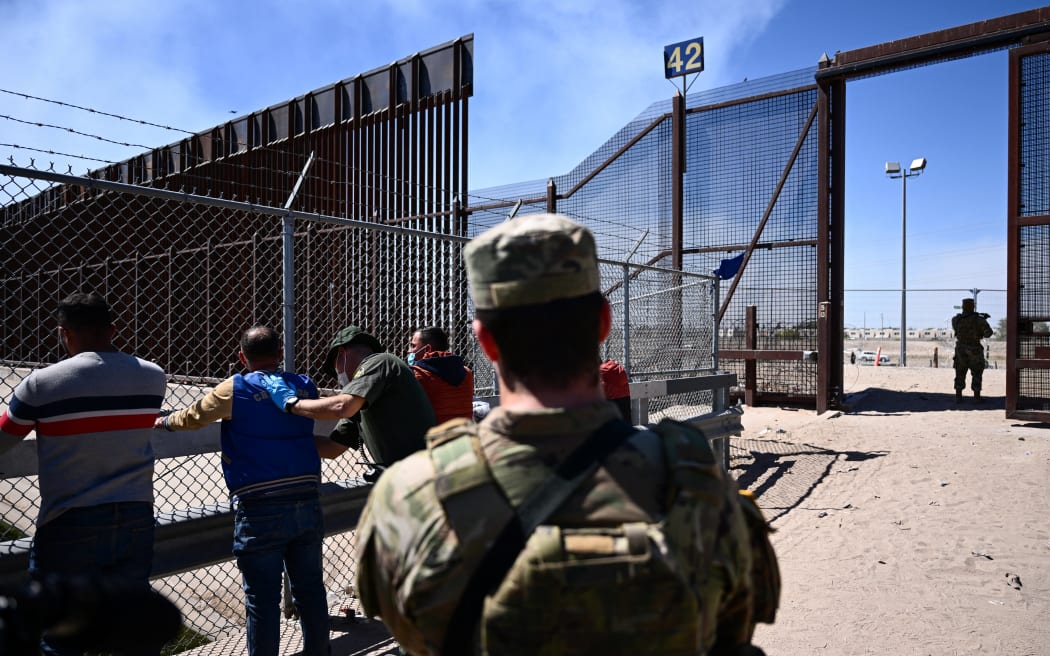 A member of the Texas Army National Guard watches as migrants are searched by a US Customs and Border Protection Border Patrol agent after surrendering themselves for the processing of immigration and asylum claims on the US-Mexico border in El Paso, Texas, on 10 May, 2023.