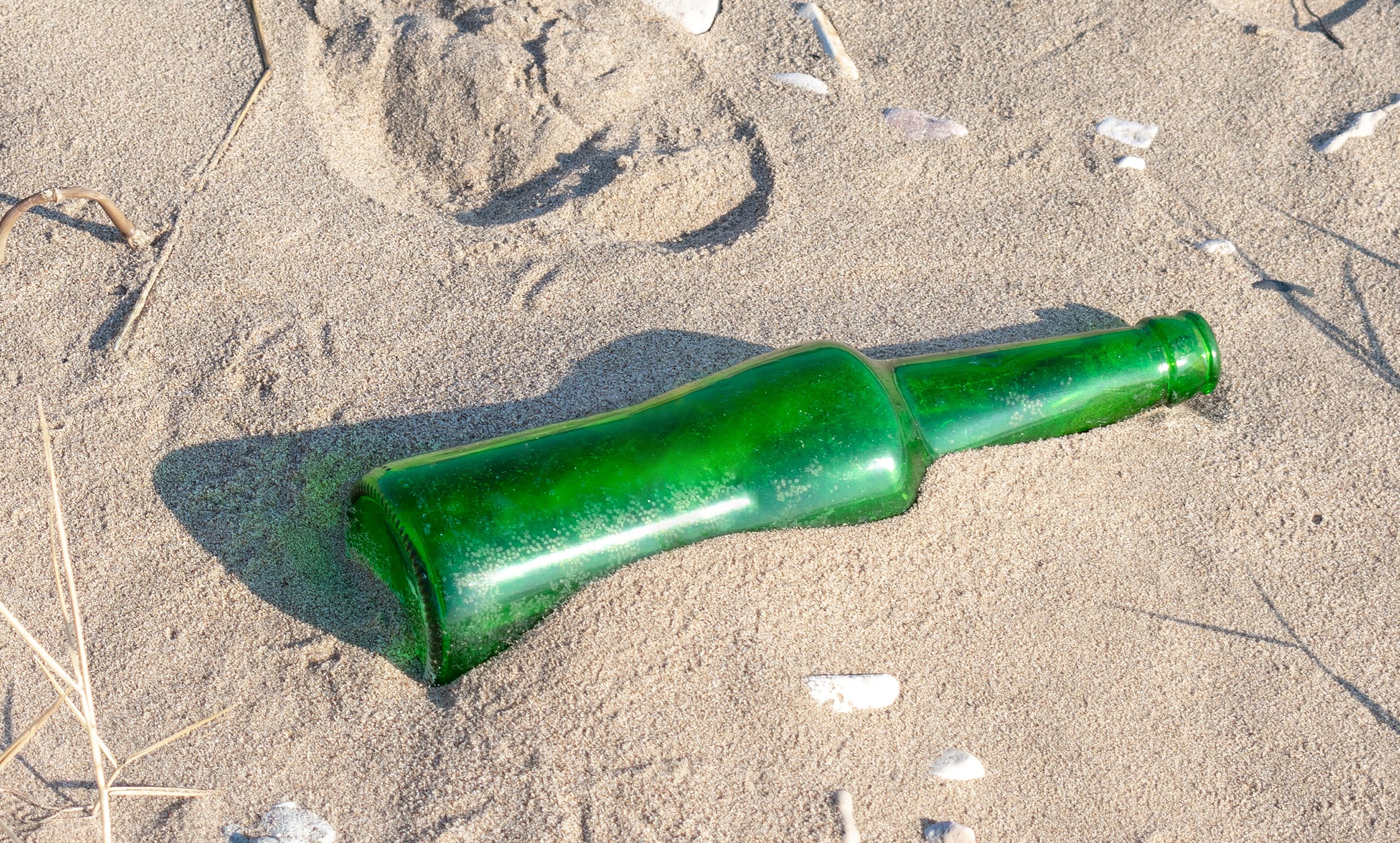 boot prints on the sand beach and man-thrown green glass bottle. concept of environmental pollution.