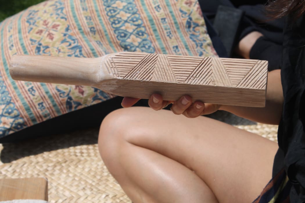 An image of artist Nikau Hindin holding one of her hand-crafted wooden beaters, used to work the wet fibre.