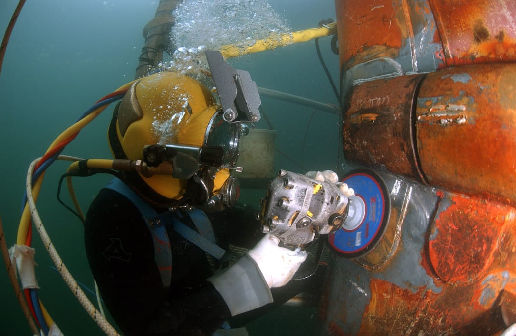 Navy diver using an angle grinder underwater on a segment of piping