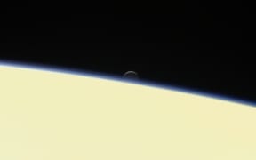 Saturn's active, ocean-bearing moon Enceladus sinks behind the giant planet in a farewell portrait from NASA's Cassini spacecraft.