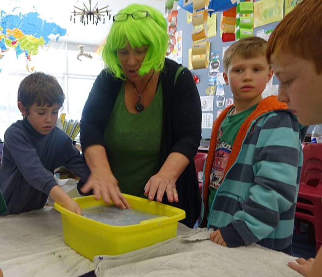 Teacher in bright green wig makes paper with a group of primary school students