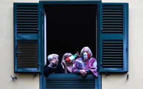 People with protective masks look from their windows at artists performing for the show Sotto lo Stesso Cielo tour (Under the Same Sky tour) in Rome on 18 April 2020.