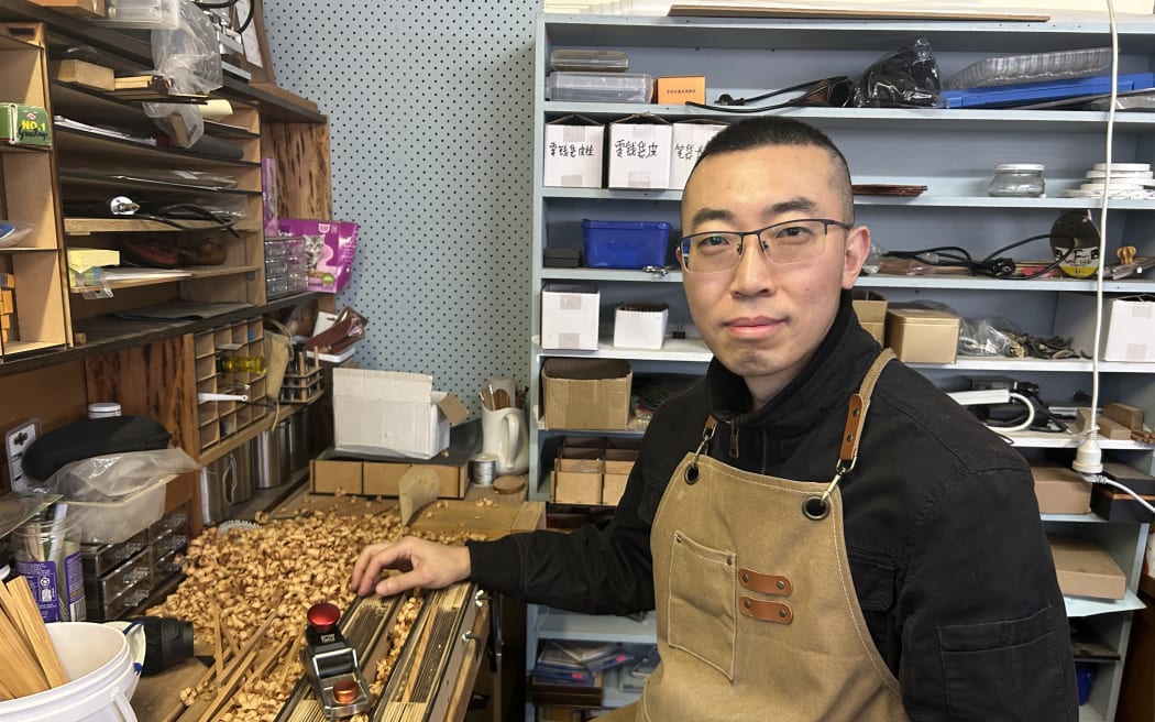 Picture shows a man smiling at the camera, with woodworking tools in the background