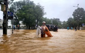 A woman wearing a raincoat wades through a flooded street in Hue on October 28, 2025. The central Vietnamese city of Hue recorded more than a metre of rainfall in a 24-hour period, smashing a national record set over two decades ago, the environment ministry said. (Photo by AFP)