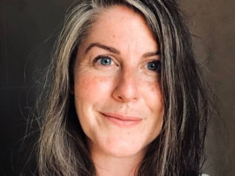 A slightly smiling woman with grey-streaked brown hair.
