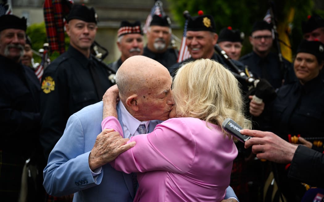 Newly-weds US WWII veteran Harold Terens, 100, (L) and Jeanne Swerlin, 96, (R) embrace in front of a piper band as they celebrate their marriage during a wedding at the town hall of Carentan-les-Marais, in Normandy, northwestern France, on 8 June, 2024.