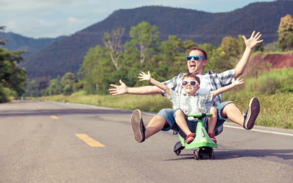 A photo of a father and son riding on a  skateboard playing on the road at the day time.