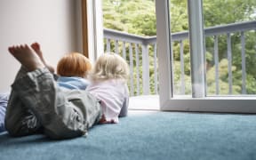 Sisters (3-6) lying on carpet looking through balcony door
