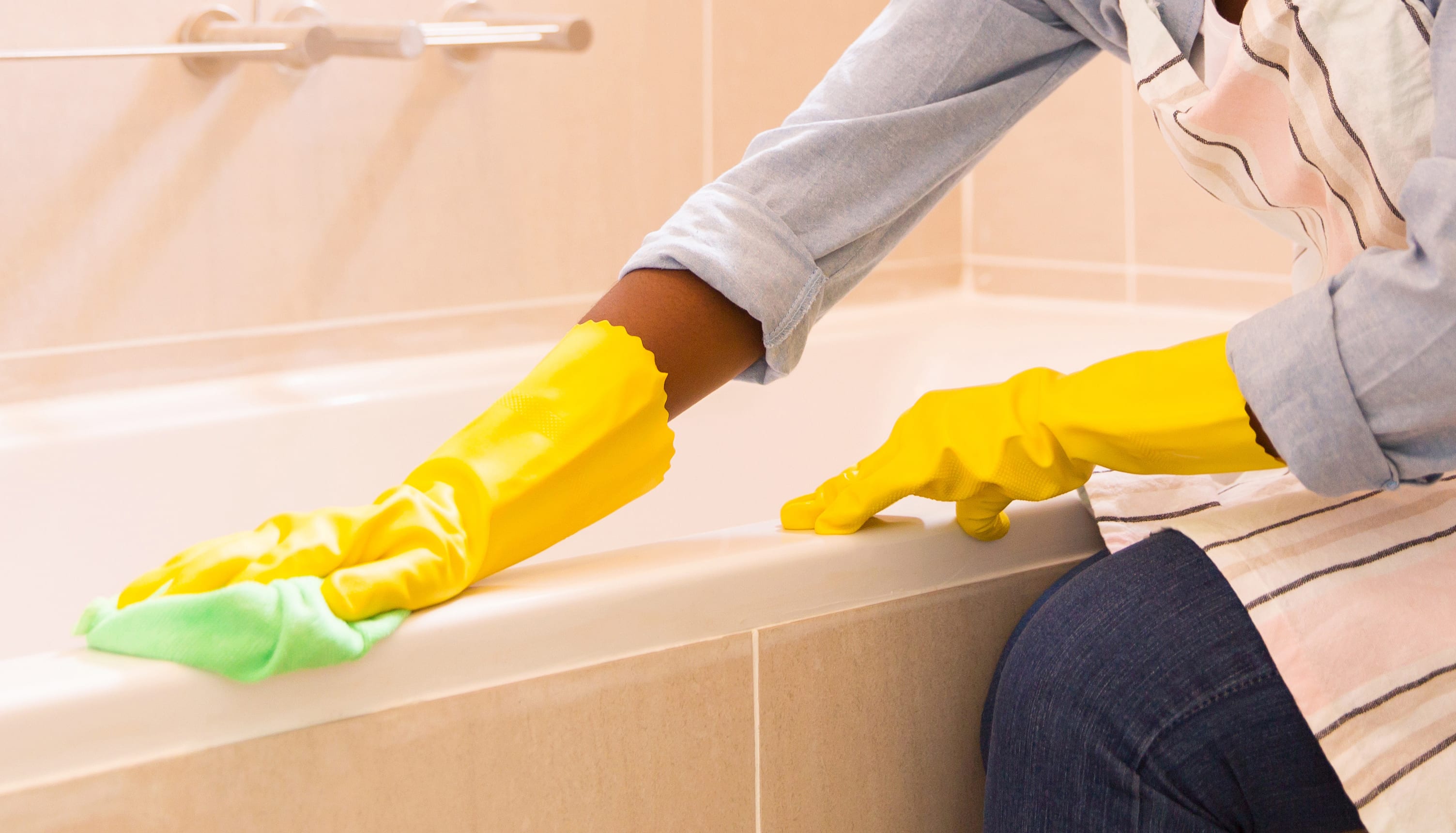 Young woman cleaning bathtub with a cloth