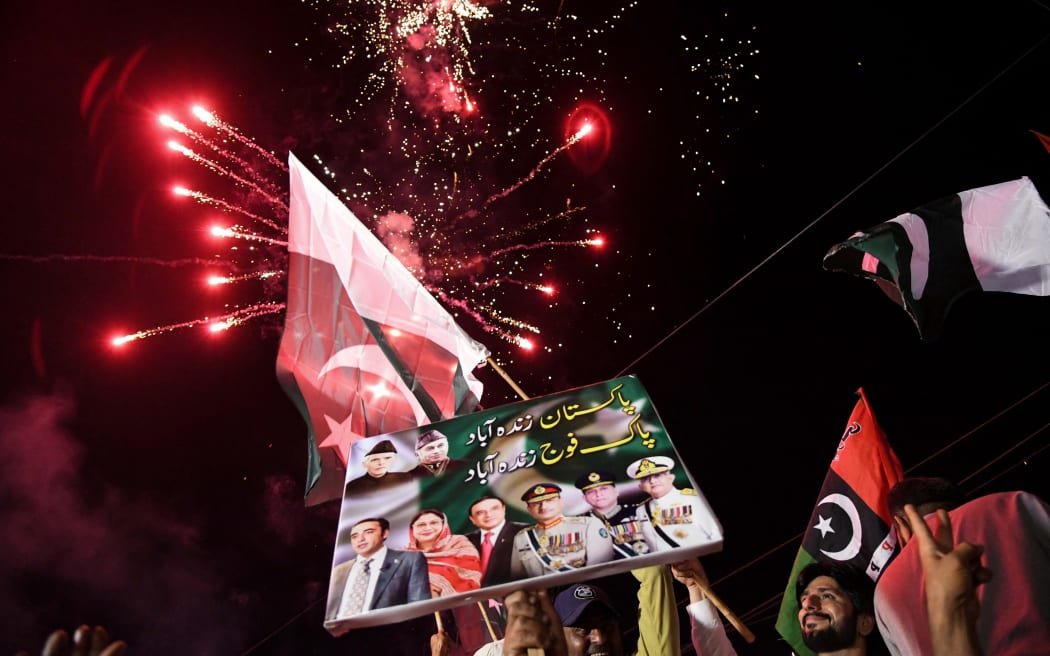 Pakistan Peoples Party (PPP) activists hold placards and wave Pakistani national flags as fireworks explode during a march expressing solidarity with the country's armed forces as they celebrate after a ceasefire between Pakistan and India, in Larkana, Sindh province on May 11, 2025. A ceasefire appeared to hold on May 11, 2025, between India and Pakistan, hours after the nuclear-armed rivals accused each other of violating a truce that brought them back from the brink of all-out war. The ceasefire was agreed on May 10, 2025, after four days of missile, drone and artillery attacks which killed at least 60 people and sent thousands fleeing, in the worst violence since India and Pakistan's last open conflict in 1999. (Photo by Ahmed Raza SOOMRO / AFP)