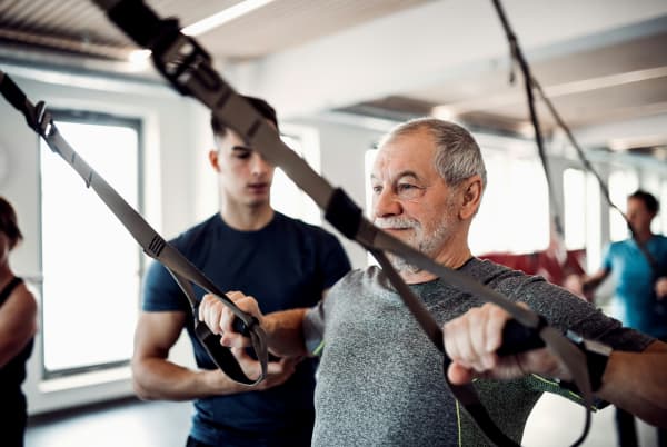 A grey haired man is helped on an exercise machine.