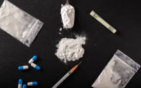 Cocaine and other drugs on a black background, close-up. A rolled up dollar bill for drug use. Prohibited drugs.
