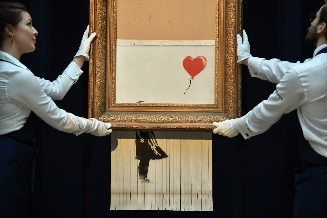 Sotheby's employees pose with the newly completed work by artist Banksy entitled "Love is in the Bin", a work that was created when the painting "Girl with Balloon" was passed through a shredder in a surprise intervention by the artist, at Sotheby's auction house in London.