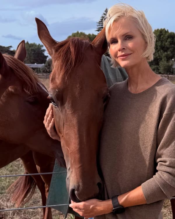 Kylie Bax - a smiling woman with a blonde bob - cradles the head of a brown horse.