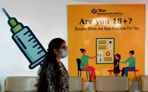 A girl walks past a poster at a vaccination centre in New Delhi on April 10, 2022, after government announced the paid precaution dose against Covid-19 coronavirus to be available for everyone above 18 years of age at private vaccination centres.