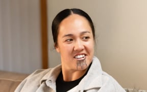 A woman with a moko kauae smiles.