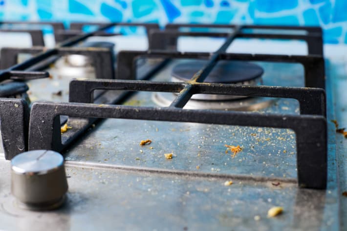 Gas stove top with food leftovers. Unclean steel kitchen cooktop with greasy spots. Spring-cleaning, remove kitchen old fat stains, fry spots, oil splatters and burned-on bits.