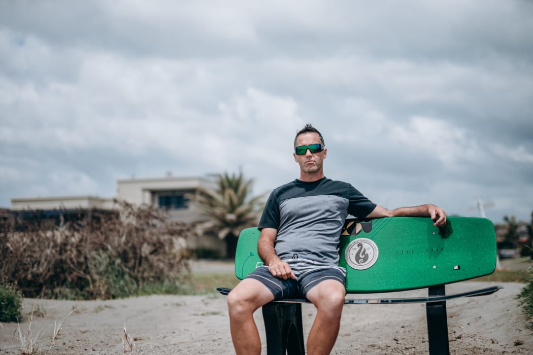 Mark Inman sit on a surfboard bench in memory of his brother tour guide Hayden Marshall-Inman whose body has not been recovered since the Whakaari White Island eruption.