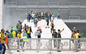 Supporters of Brazilian former President Jair Bolsonaro clash with the police during a demonstration outside Brazil's National Congress headquarters in Brasilia on January 8, 2023. - Brazilian police used tear gas Sunday to repel hundreds of supporters of far-right ex-president Jair Bolsonaro after they stormed onto Congress grounds one week after President Luis Inacio Lula da Silva's inauguration, an AFP photographer witnessed. (Photo by EVARISTO SA / AFP)