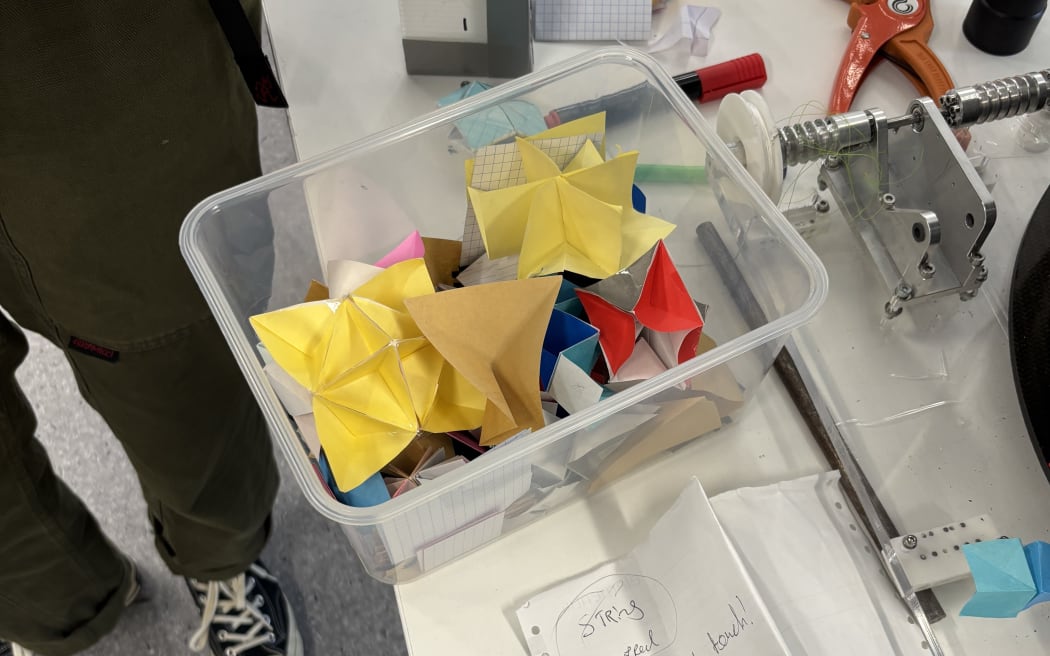 A plastic box containing many potential designs for the SAR4SaR search and rescue device, folded from coloured origami paper.