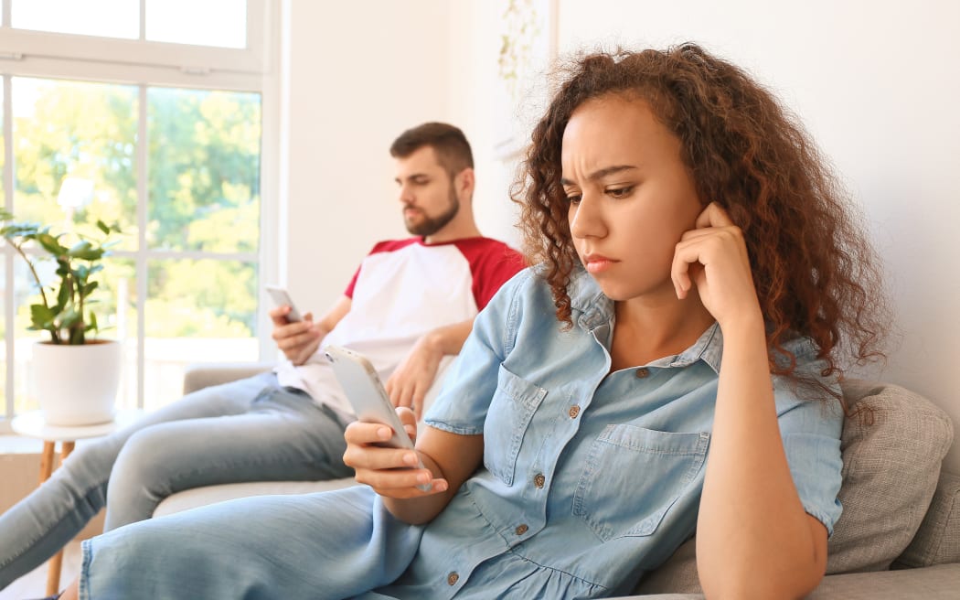 Young couple with mobile phones on sofa at home.