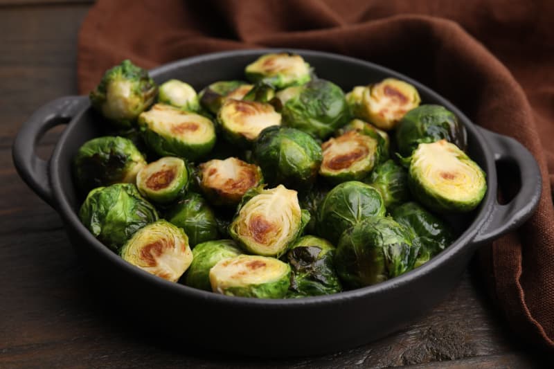 Delicious roasted Brussels sprouts in baking dish on wooden table, closeup.