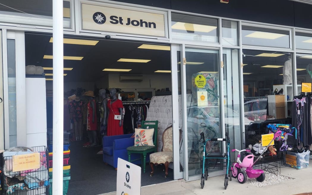 Picture shows the store front of an op shop. The display includes racks of clothing items, children's toys and books.