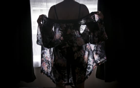 Woman stands silhouetted against window in lingeries and drapy wrap
