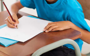 A young boy writes at a desk at a primary school.