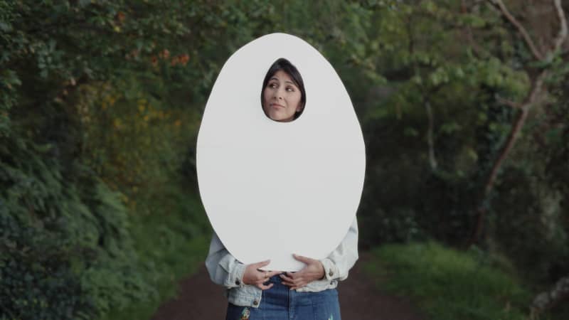Director Shamin Yazdani holds up a cardboard cutout of an egg shape.