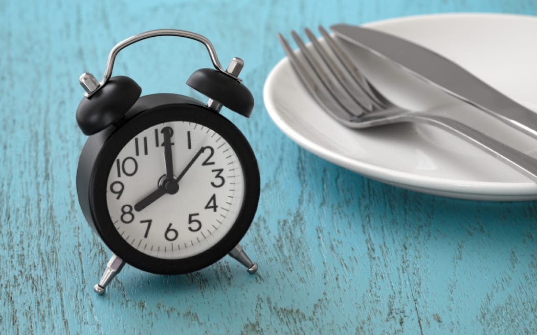 Clock with fork and knife on white plate, intermittent fasting, meal plan, weight loss concept