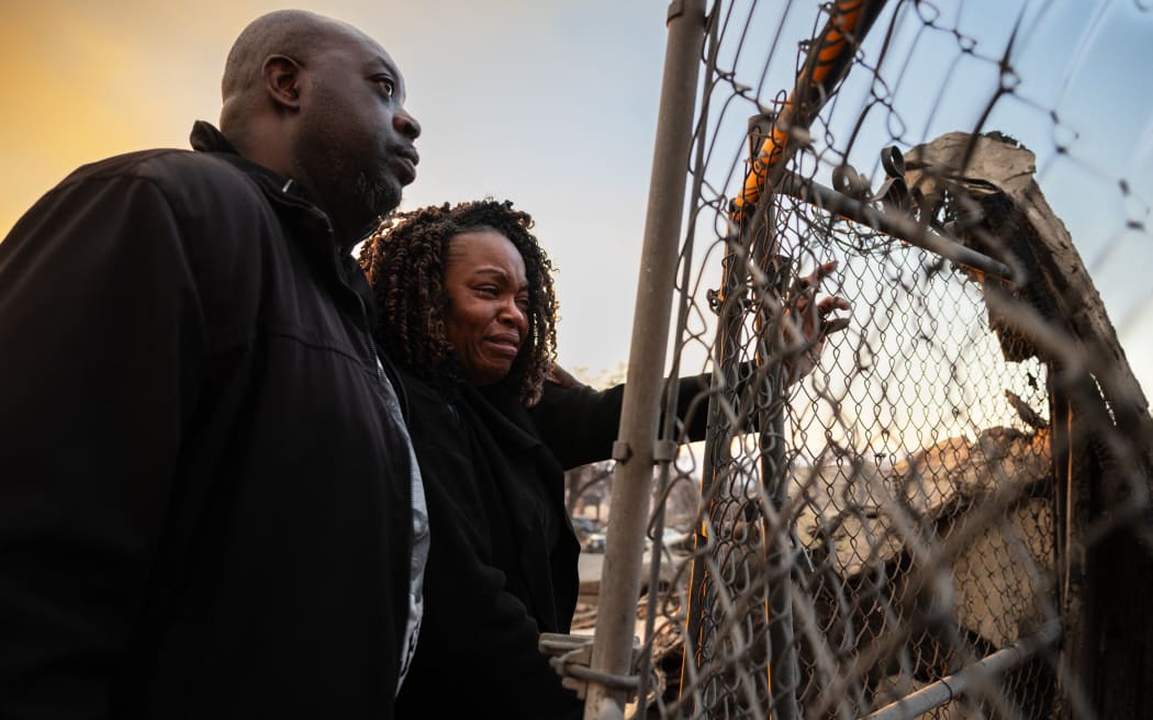 A couple looks at the charred remains of their home burned in the Eaton Fire in Altadena, California, January 9, 2025. Massive wildfires that engulfed whole neighborhoods and displaced thousands in Los Angeles remained totally uncontained January 9, 2025, authorities said, as US National Guard soldiers readied to hit the streets to help quell disorder. Swaths of the United States' second-largest city lay in ruins, with smoke blanketing the sky and an acrid smell pervading almost every building. (Photo by Zoë Meyers / AFP)