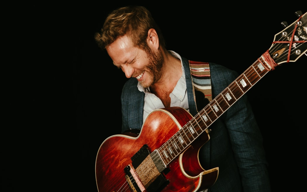 Guitarist Rotem Sivan with his red archtop guitar, looking down to the side and laughing