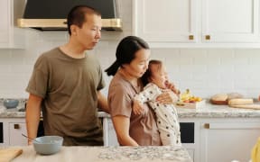An Asisn woman holds a baby while the father looks on.