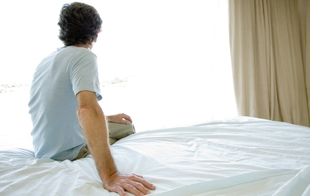 Mature man sitting alone on bed, looking out window (Photo by Eric Audras / AltoPress / PhotoAlto via AFP)