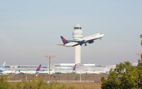 ATLANTA, GEORGIA - NOVEMBER 7: A plane flies past the air traffic control tower as people travel through Hartsfield-Jackson Atlanta International Airport on November 7, 2025 in Atlanta, Georgia. Today marks day 38 of the government shutdown.   Megan Varner/Getty Images/AFP (Photo by Megan Varner / GETTY IMAGES NORTH AMERICA / Getty Images via AFP)