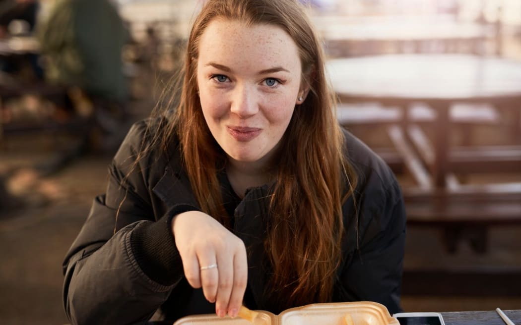 Portrait of young woman, outdoors, eating chips, Bristol, UK
