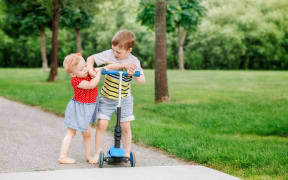 A photo of two little Caucasian preschool children fighting hitting each other. Boy and girl can not share one scooter. Older sibling brother not giving his toy to younger sister. Communication problems.