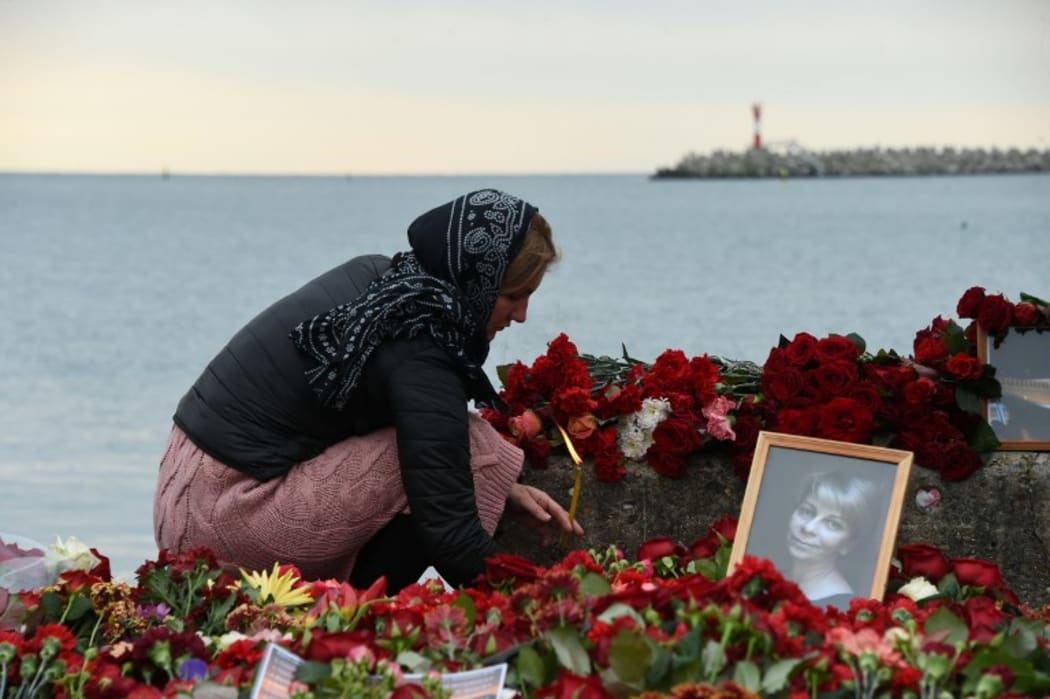 A woman lights a candle next to flowers and a portrait of one of the victims, famous Russian charity activist and founder of the Voters' League Elizaveta Glinka or Dr Liza, at a makeshift memorial at the embankment on the shore of the Black Sea in Sochi.