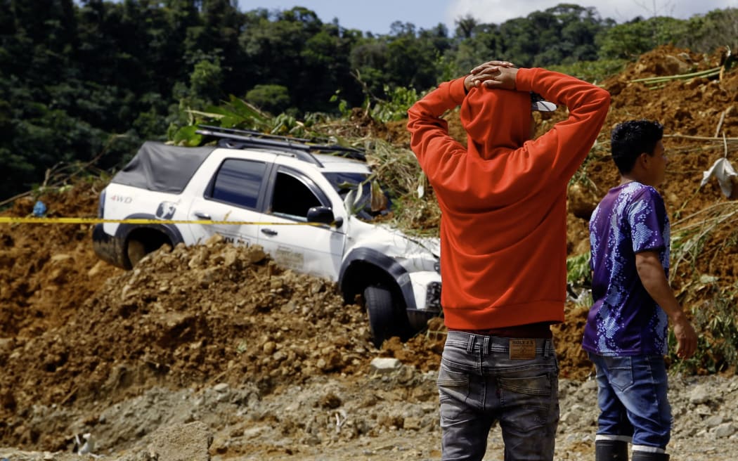 People stand in the area of a landslide in the road between Quibdo and Medellin, Choco department, Colombia on January 13, 2024. At least 23 people were killed and around 20 are injured after a landslide in an indigenous community in northwestern Colombia, an official from the Choco department governor's office told AFP. (Photo by Fredy BUILES / AFP)