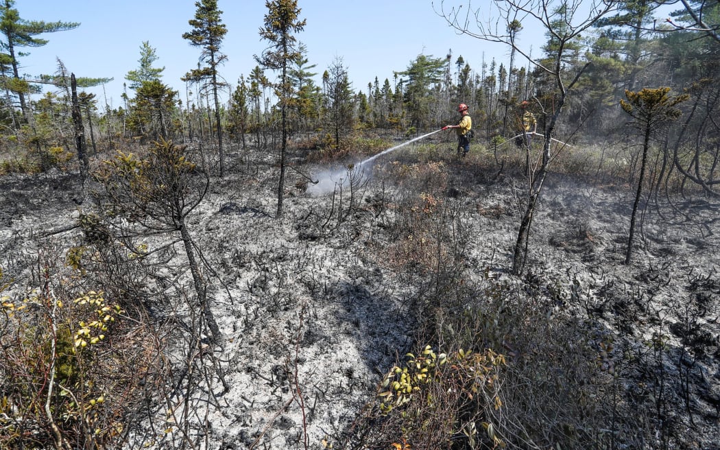 Firefighters Walter Scott and Zac Simpson hose down the ground around Barrington Lake, Shelburne county, Canada, on 1 June 2023. Image courtesy of the Nova Scotia Government.